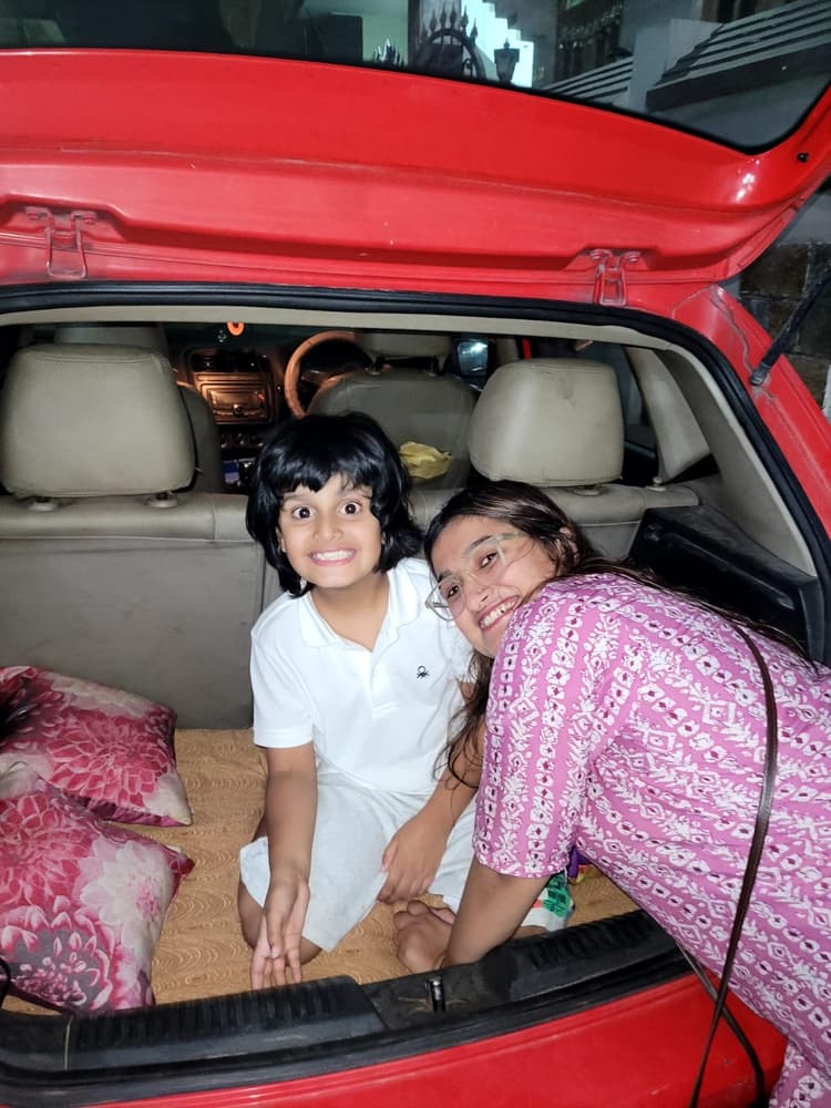 Vyom sitting in the open red car trunk with cushions, smiling with adventurous excitement